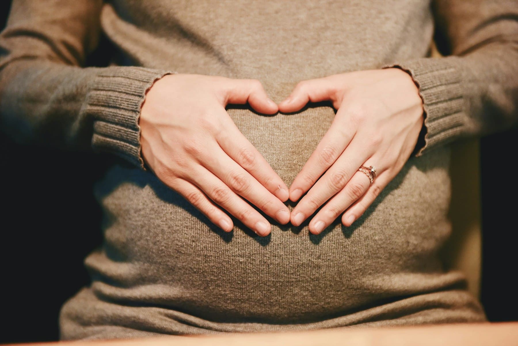 Mâinile unei femei însărcinate, așezate pe abdomen peste un pulover tricotat